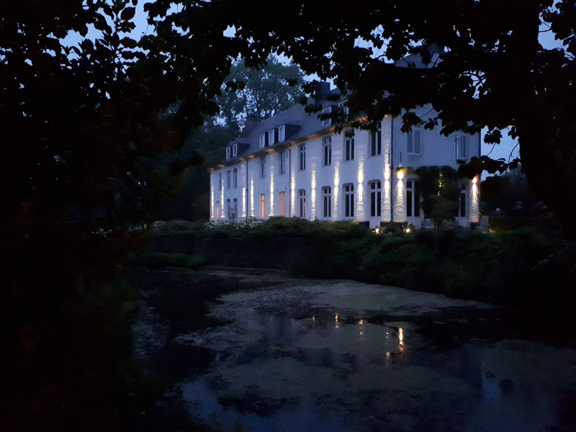 A white manor house lit by brass wall uplights at dusk
